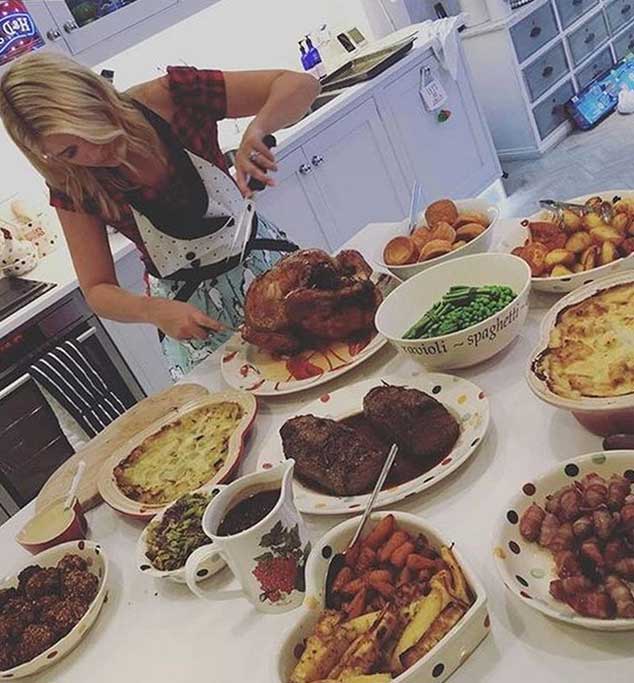 A woman carving a roast turkey at a table laden with a large spread of food.