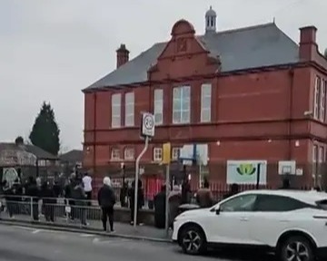 People gathered outside a brick school building.