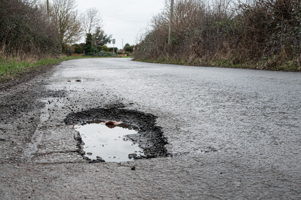 Large pothole filled with rainwater on a rural road.