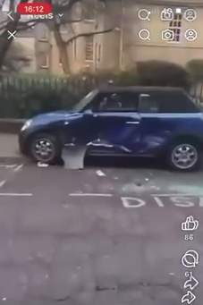 A damaged blue Mini Cooper parked on a street.