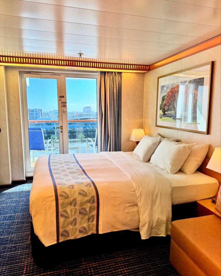 Cruise ship stateroom with a bed, balcony view, and artwork.