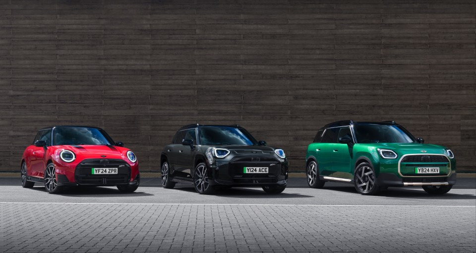 Three Mini Coopers in red, black, and green parked in front of a wooden wall.