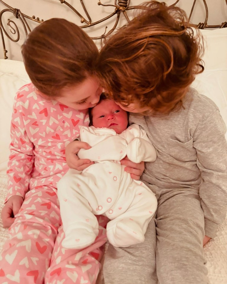 Two children kissing a newborn baby.