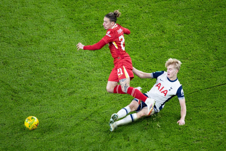 A soccer player from Liverpool tackles a Tottenham Hotspur player.