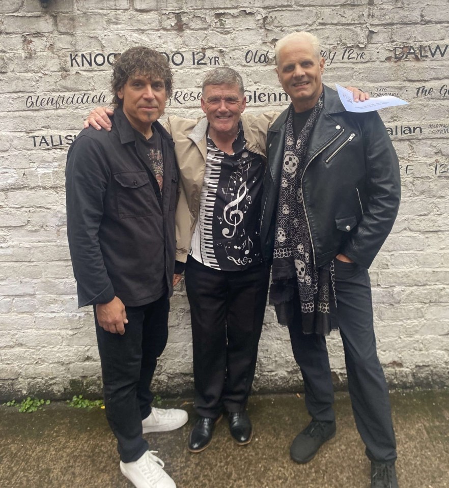 Three men posing for a photo in front of a brick wall.