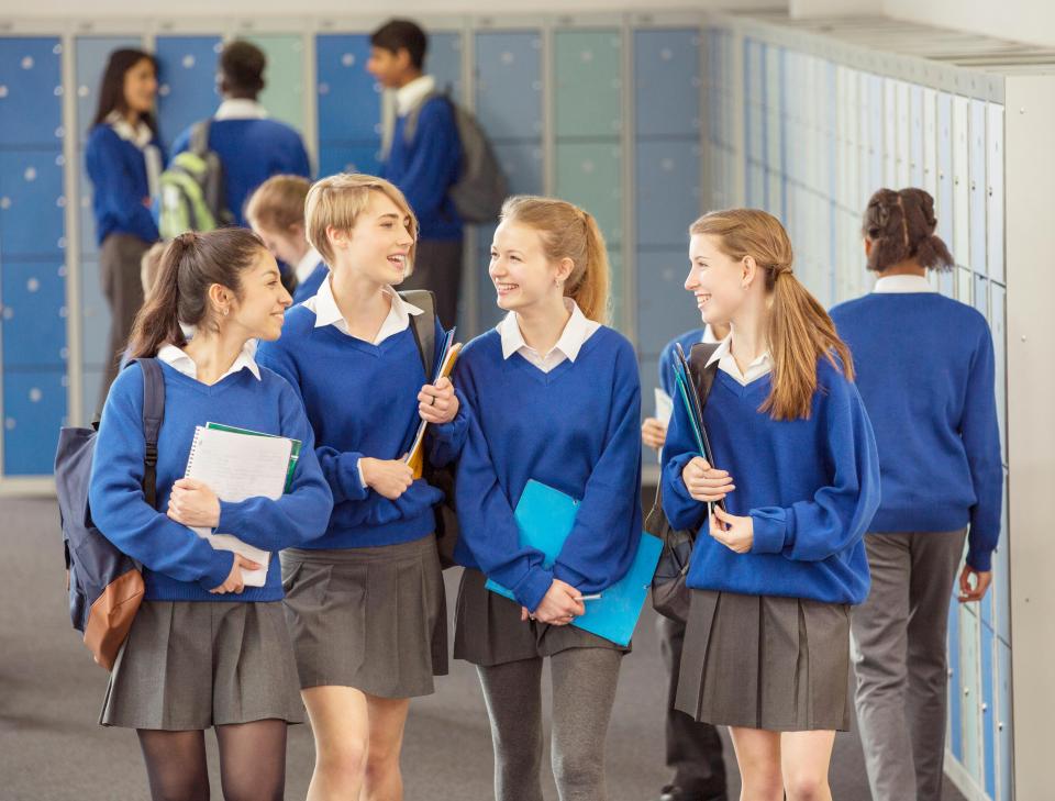 Four female students in blue uniforms chat in a school hallway.