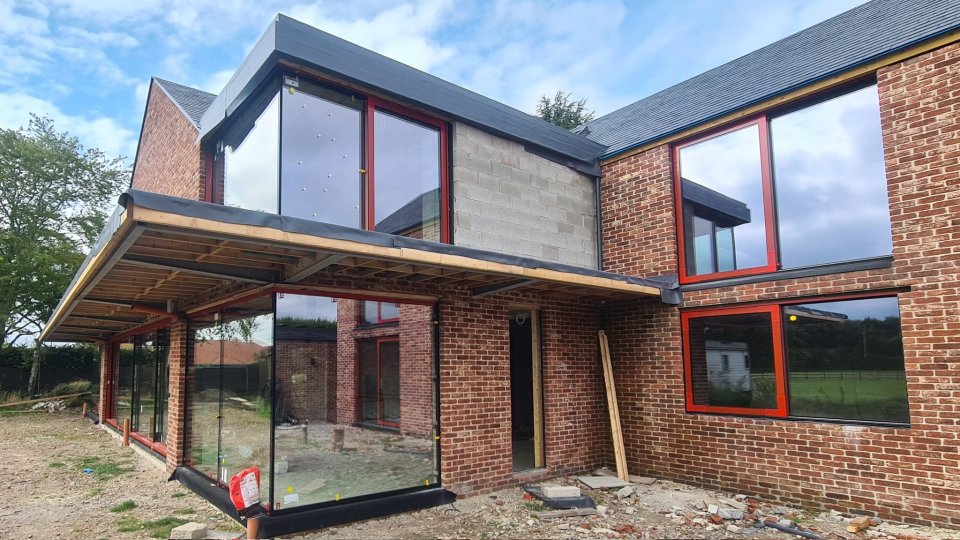 A brick house under construction, featuring large windows with red frames.