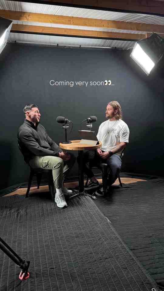 Two men sitting opposite each other in a podcast studio; "Coming very soon..." text is visible on the wall behind them.