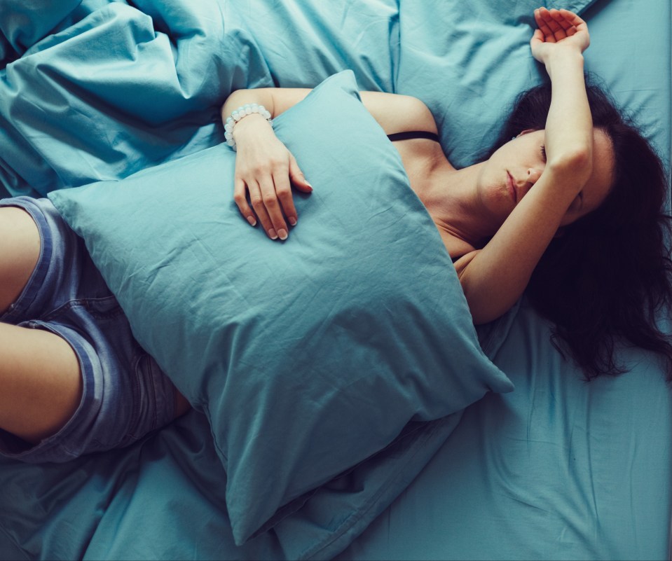 A depressed woman lying in bed with her hand on her forehead.