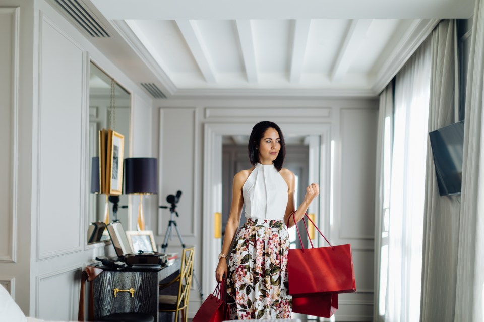 Woman carrying shopping bags in a hotel hallway.