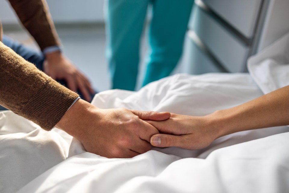 Close-up of a couple holding hands in a hospital bed.