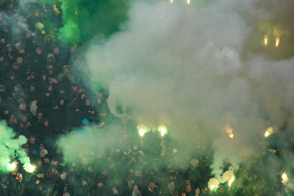 Feyenoord fans igniting green flares at a soccer match.