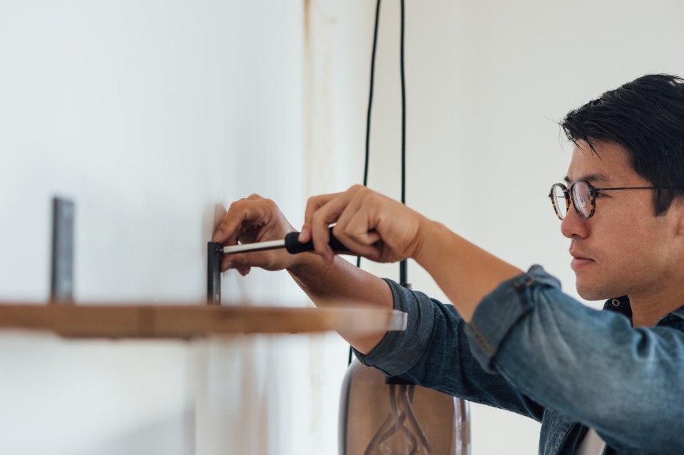 A man uses a screwdriver to install a shelf.