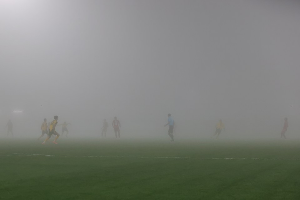 Soccer players on a foggy field.