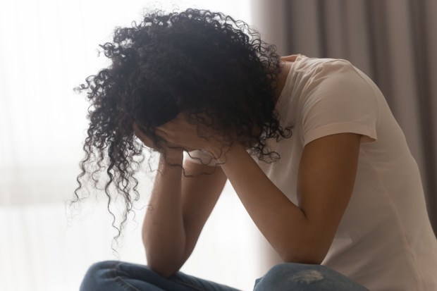 A young Black woman sits with her head in her hands, appearing upset.