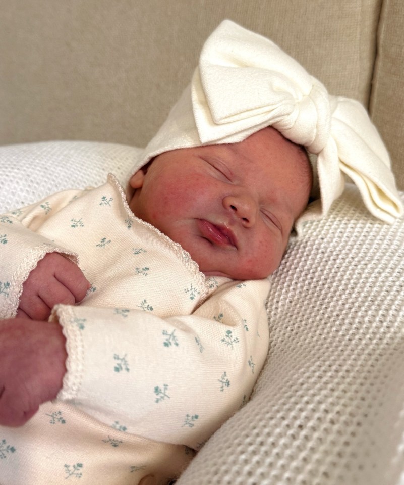 Sleeping newborn wearing a white bow headband.