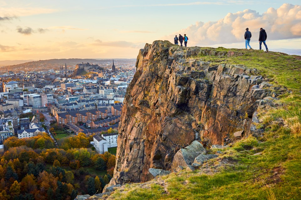 People overlooking Edinburgh from a clifftop at sunset.