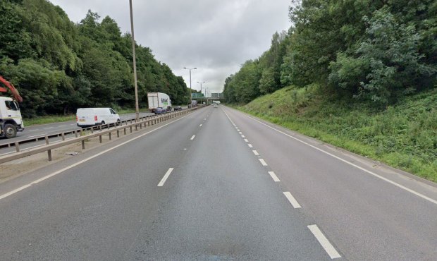 Multi-lane highway with few vehicles, lined with trees.