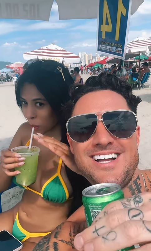 Couple on a beach; one is drinking a green beverage.