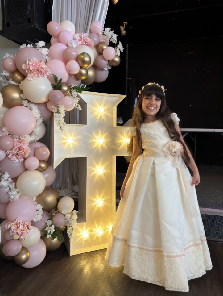 Girl in white dress standing next to lighted cross.