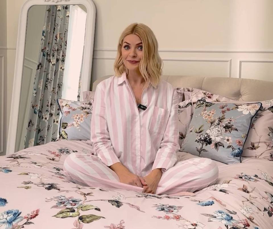 Holly Willoughby sitting on a bed in pink striped pajamas.