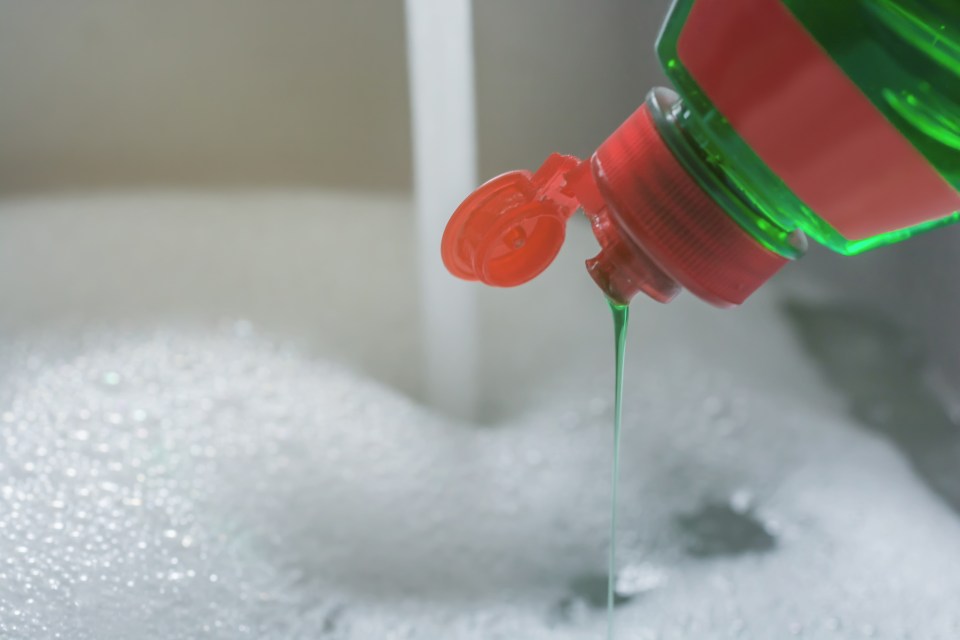 Green dish soap being poured into a sink of soapy water.