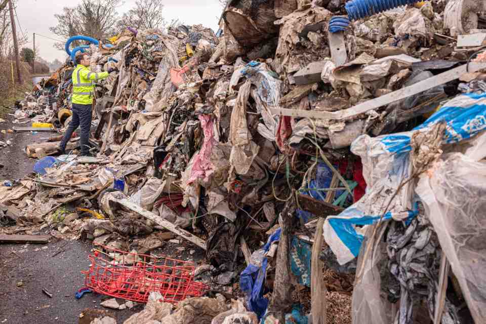 A worker surveys a large pile of fly-tipped rubbish.