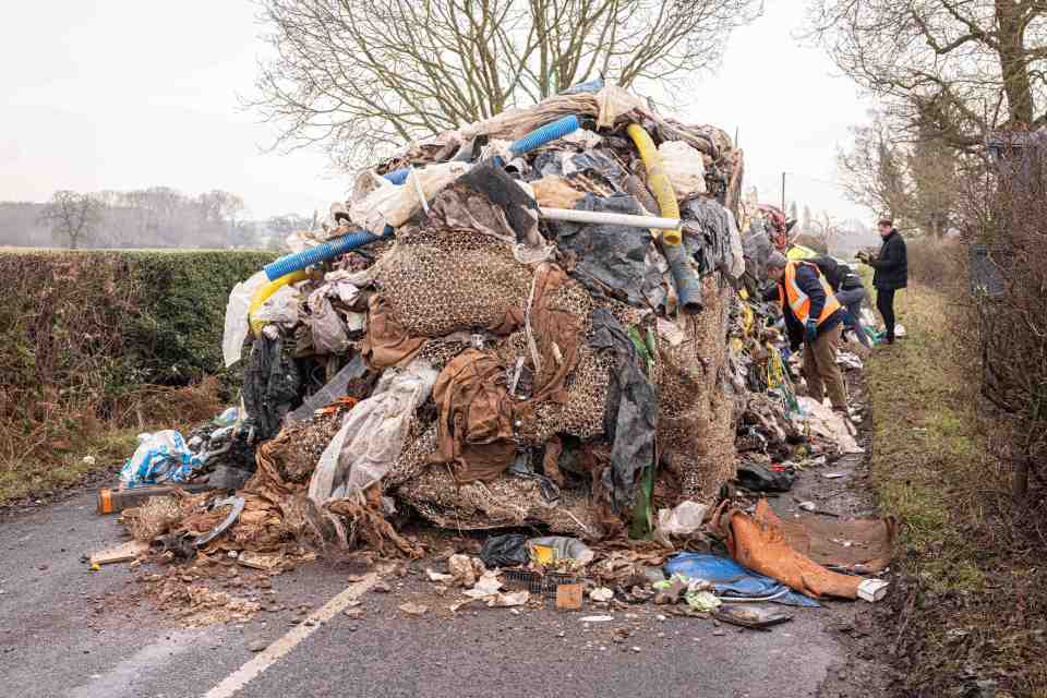 A large pile of fly-tipped rubbish on a roadside.