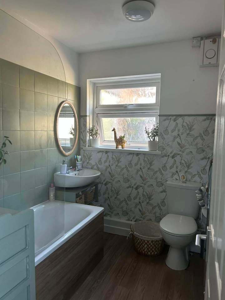 Renovated bathroom with green tile, tropical wallpaper, and wood-paneled bathtub.