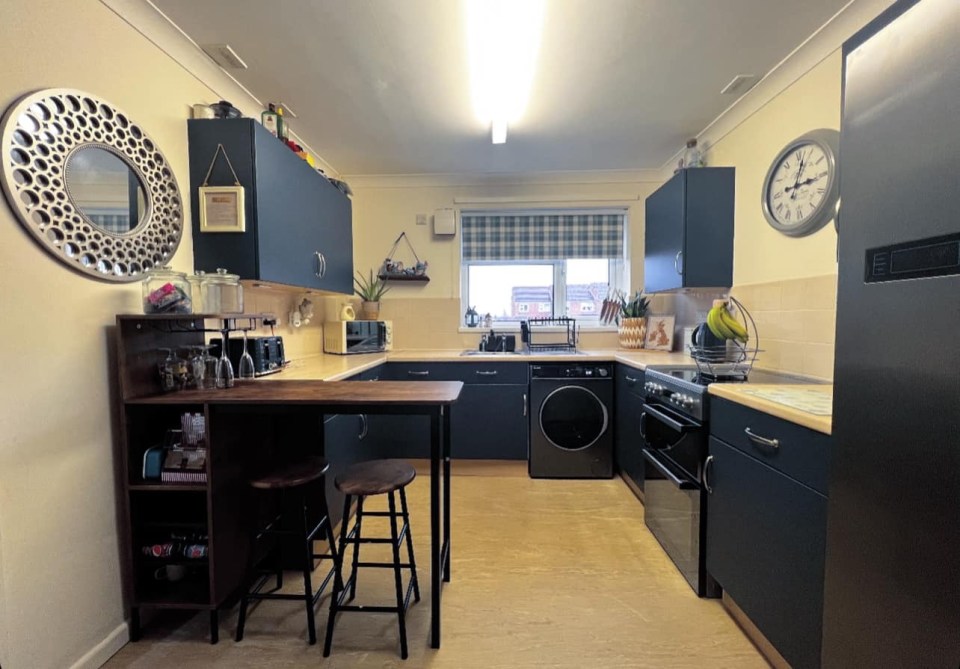 Renovated council house kitchen with dark blue cabinets and new appliances.