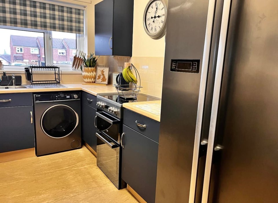 Renovated council house kitchen with dark blue cabinets, new appliances, and light wood flooring.