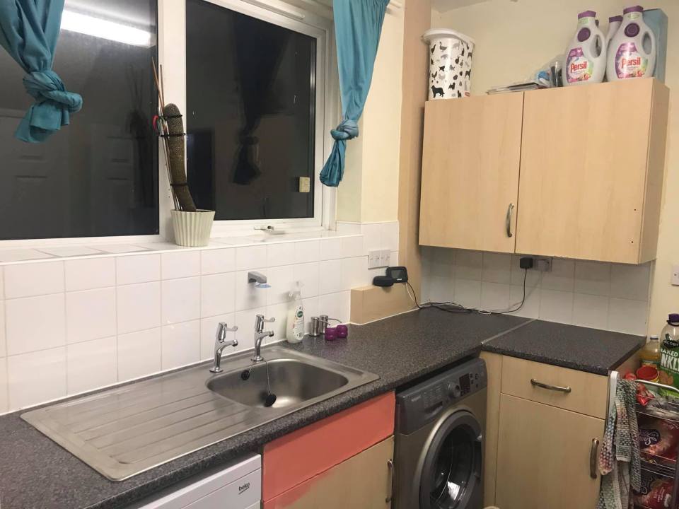 A small kitchen with light wood cabinets, a stainless steel sink, and a washing machine.