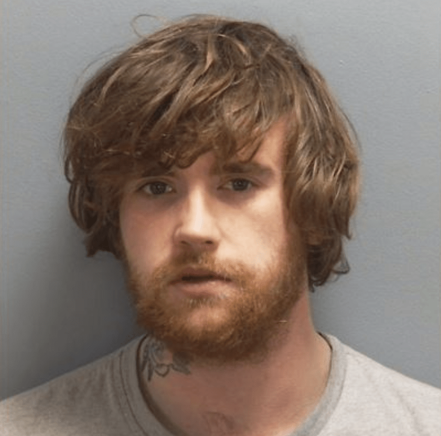 Mugshot of a man with light brown, wavy hair and a red beard.