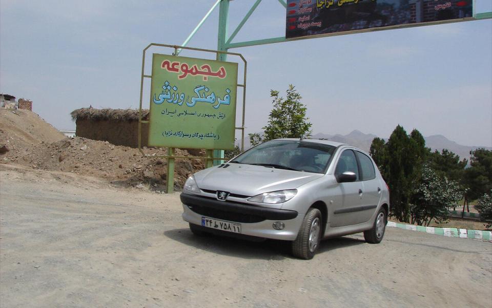 Silver Peugeot 206 parked near a sign in Farsi.