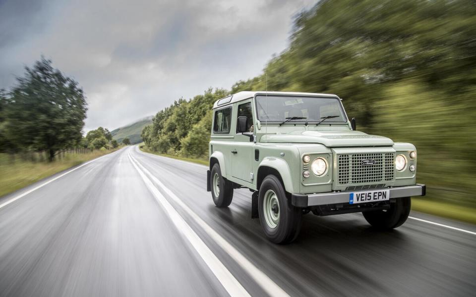 Light green Land Rover Defender driving on a road.