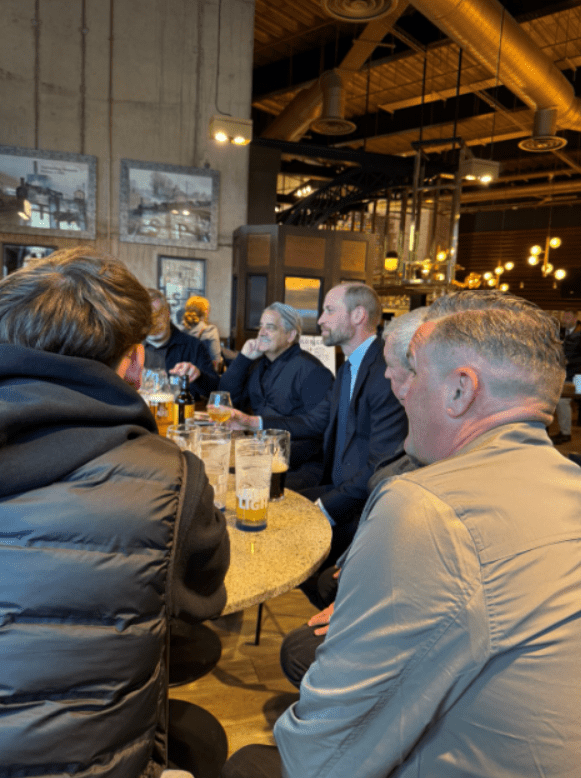 Group of men seated around a table, drinking beer.