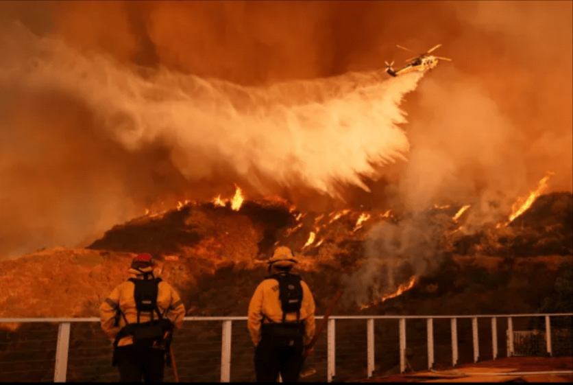 Firefighters watch as a helicopter drops water on a wildfire.