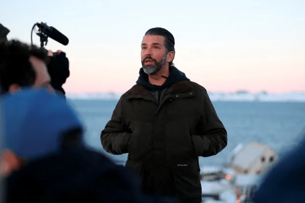 Man in dark jacket being interviewed outdoors.