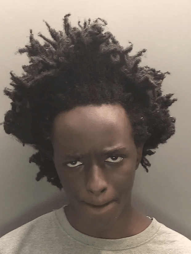 Mugshot of a person with dark skin and locs.