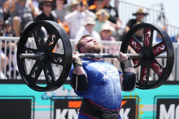 Strongman competitor performing a shoulder press with a heavy barbell.