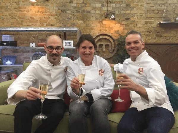 Three chefs in white jackets toasting with champagne flutes.