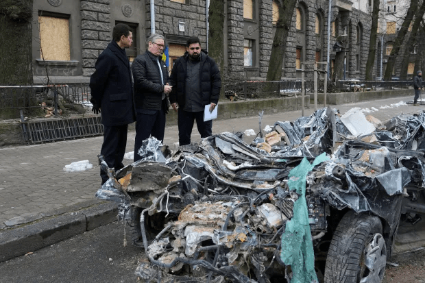 Three men examining a severely damaged car.