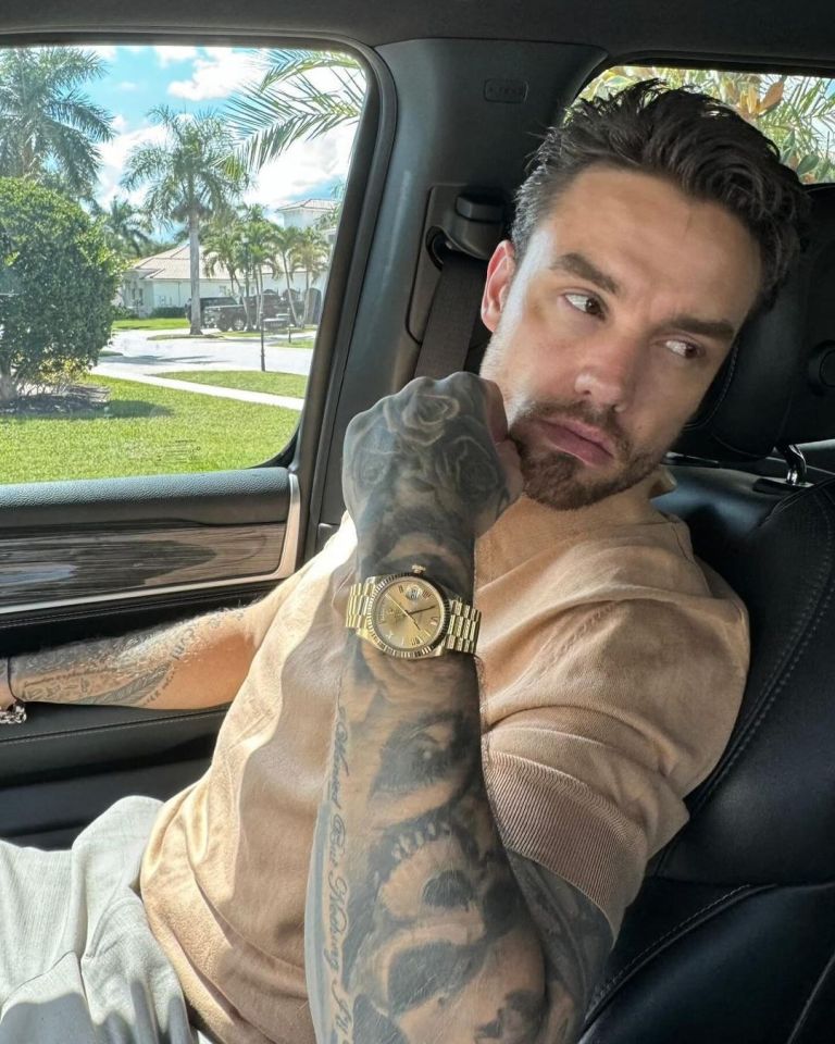 Man with tattoos wearing a gold watch sits in a car.