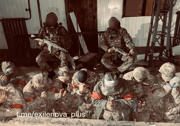 Soldiers with rifles guarding kneeling prisoners.