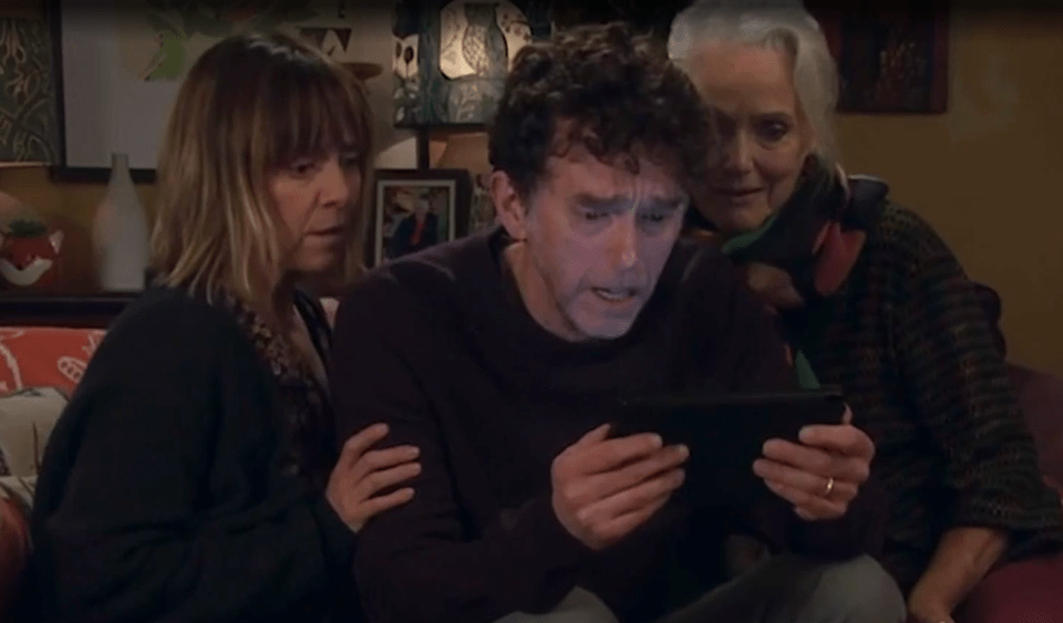 A man looks at a tablet while two women look on.