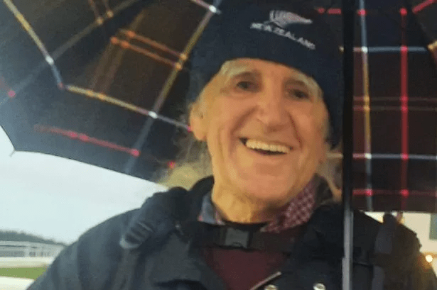 Smiling older man under an umbrella.