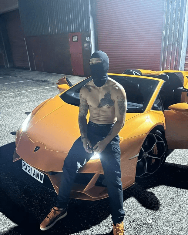 Man in balaclava sitting on orange Lamborghini.