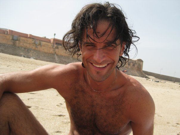 Shirtless man smiling on a beach.