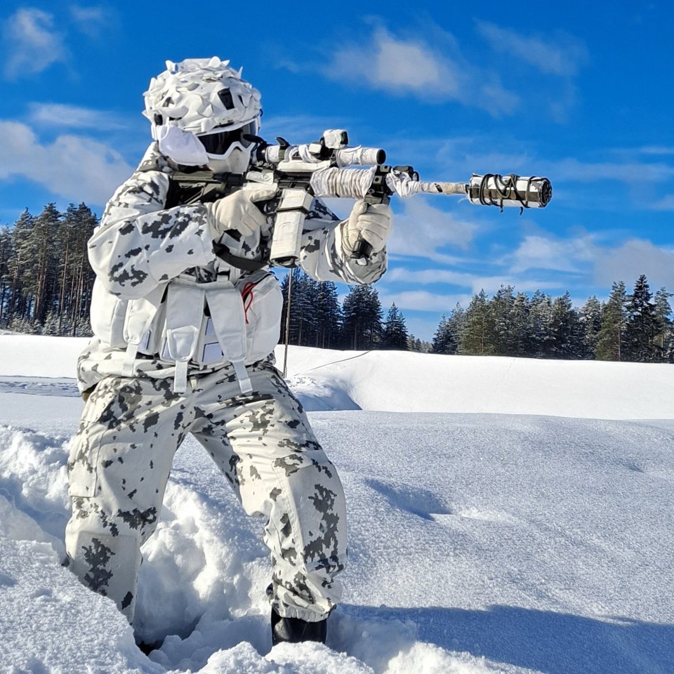 Soldier in snowy camouflage aiming a rifle.