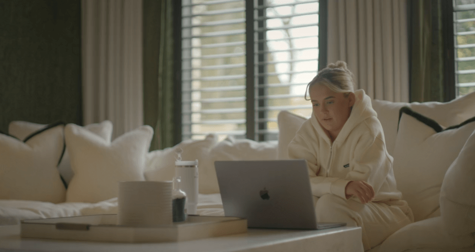 Woman in a cream hoodie using a laptop on a couch.